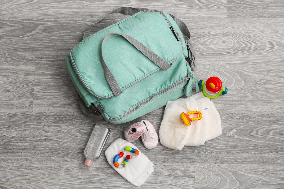 A changing bag on the floor with baby clothes, a bottle and toys