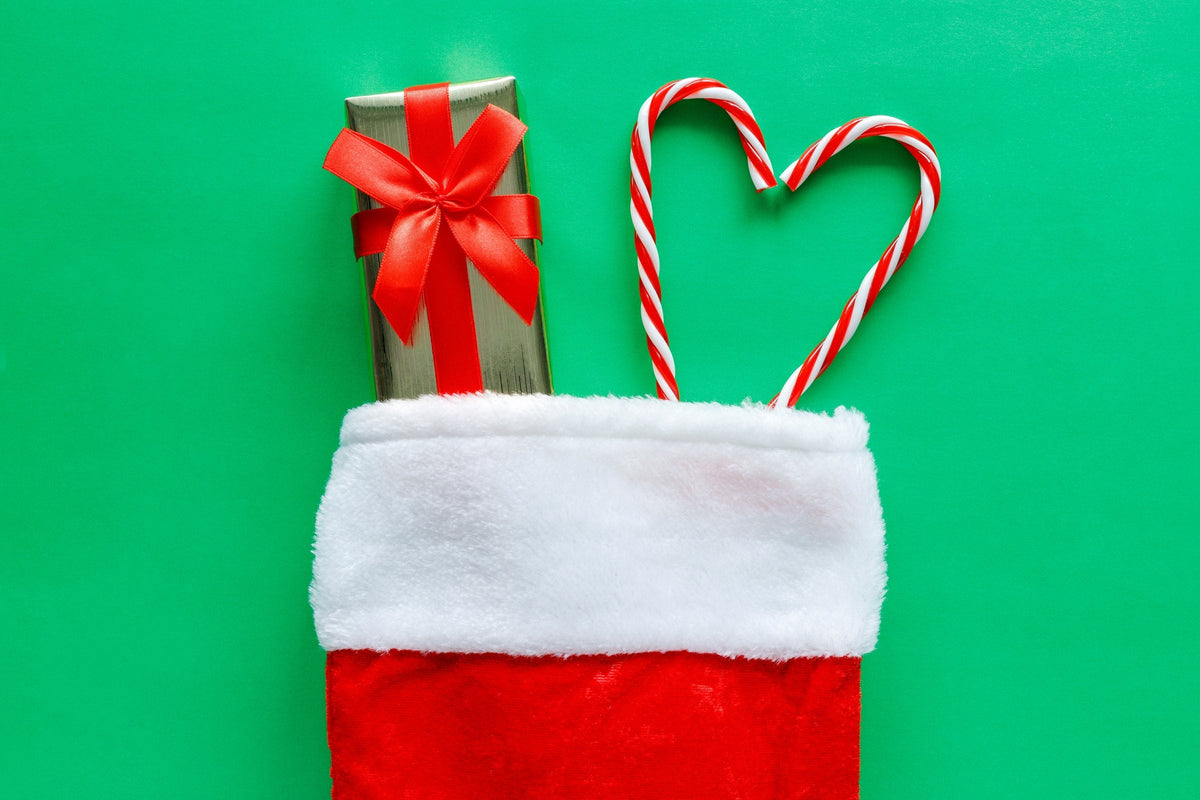 A Christmas stocking with a small gift box and candy canes on a green background